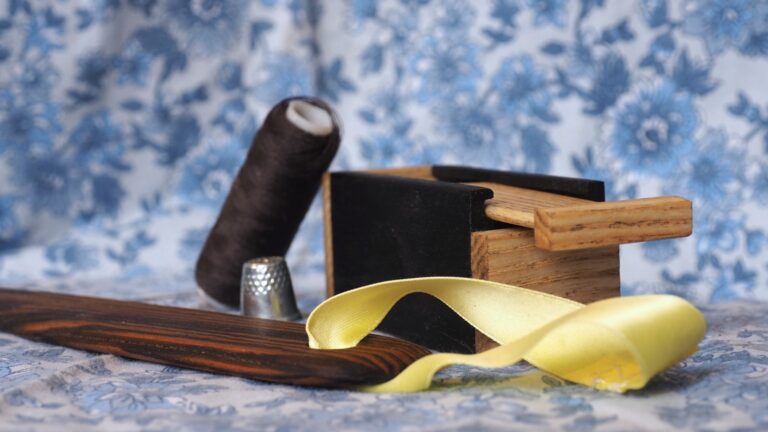 Photo d'un kit de couture en gros plan : une petite boite à aiguille en ébène et en frêne et un plioir dau bois d'un marron chaud avec des veines très marquées.