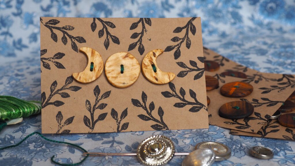 Une plaque de boutons en gros plan, ce sont trois boutons en bois assez clair, d'un jaune clair tirant sur le miel. Les trois boutons forment les phases de la lune, une lune croissante, une pleine lune et une lune décroissante.